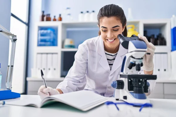 Young Beautiful Hispanic Woman Scientist Using Microscope Writing Notebook Laboratory — Stock Photo, Image