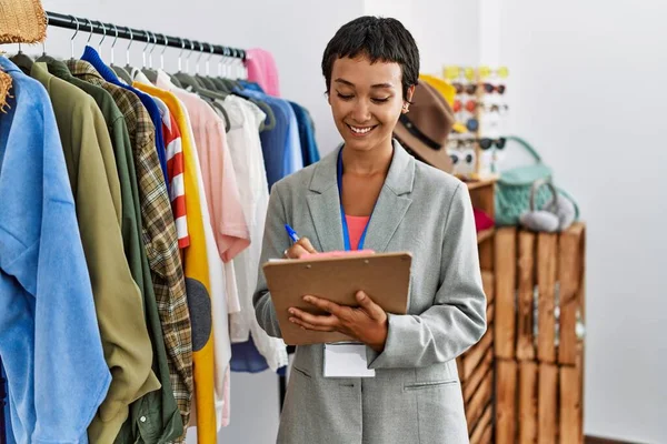 Joven Comerciante Hispana Sonriendo Confiada Escritura Portapapeles Tienda Ropa —  Fotos de Stock