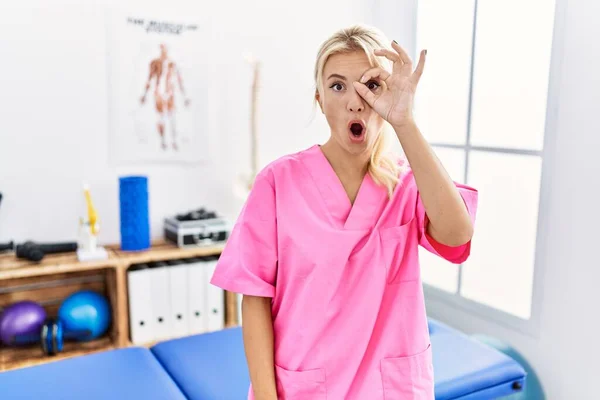 年轻的高加索女人在疼痛恢复诊所工作时 做着一个很好的姿势 满脸惊讶 用手指看着 不信的表情 — 图库照片