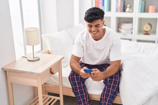 Young Hispanic Man Using Smartphone Sitting Bed Bedroom — стоковое фото