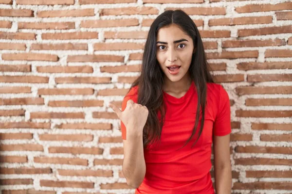 Young Teenager Girl Standing Bricks Wall Surprised Pointing Hand Finger — Stockfoto