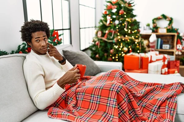 Joven Afroamericano Sentado Sofá Bebiendo Café Junto Árbol Navidad Apuntando — Foto de Stock