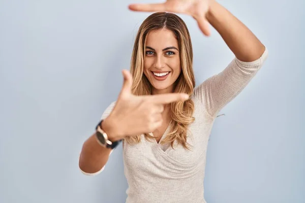 孤立した背景に立つ若いブロンドの女性は 幸せな顔をした手と指でフレームを作ります 創造性と写真の概念 — ストック写真