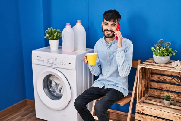 Joven Hispano Hablando Smartphone Bebiendo Café Esperando Lavadora Lavandería — Foto de Stock