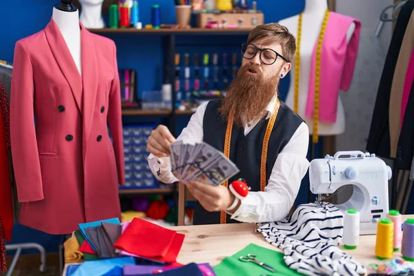 Young redhead man tailor holding dollars at clothing factory