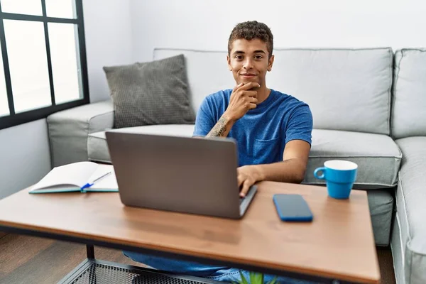 若いハンサムなヒスパニック系の男性は 床の上に座っているノートパソコンを使用して交差腕と手をあごに提起笑顔でカメラを見て自信を持っている ポジティブな — ストック写真
