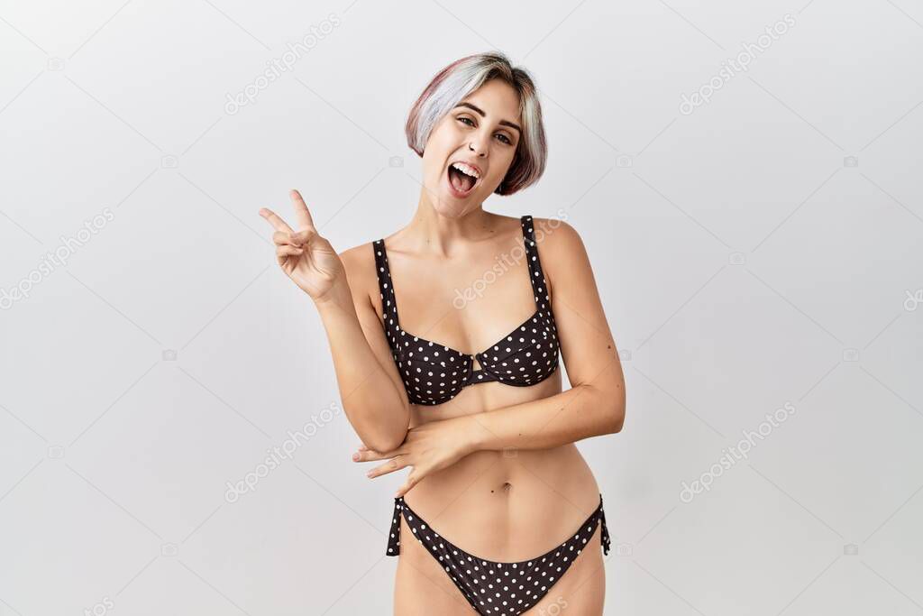 Young beautiful woman wearing swimsuit over isolated background smiling with happy face winking at the camera doing victory sign with fingers. number two. 