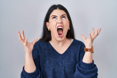 Genç esmer kadın izole arka planda duruyor. Deli gibi bağırıyor, agresif bir ifadeyle bağırıyor ve kollarını kaldırıyor. hüsran kavramı. 