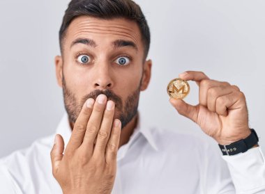 Monero kripto bozuk para tutan yakışıklı İspanyol bir adam. Ağzını eliyle kapatıyor. Şok olmuş ve hata yapmaktan korkuyor. şaşırmış ifade 
