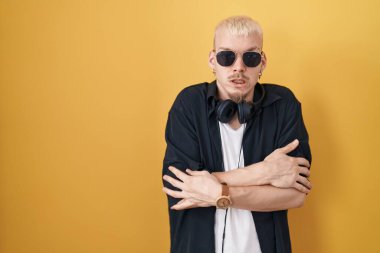 Sarı arka planda duran, güneş gözlüğü takan genç, beyaz bir adam. Kış soğuğu yüzünden titriyor ve donuyor. Yüzünde üzgün ve şok ifadesi var. 