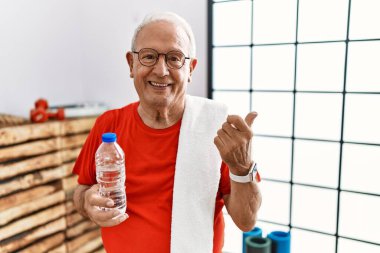 Senior man wearing sportswear and towel at the gym cheerful with a smile on face pointing with hand and finger up to the side with happy and natural expression 