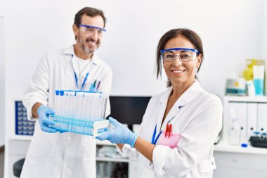 Laboratuvarda deney tüpü tutan bilim adamı üniforması giyen orta yaşlı erkek ve kadın partnerler.