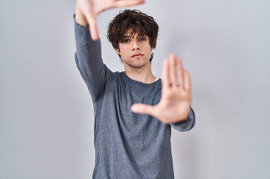 İzole edilmiş arka planda duran genç adam el ve parmakları kullanarak kare yapıyor, kamera perspektifi kullanıyor. 