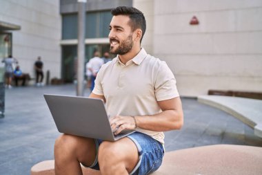 Sokakta dizüstü bilgisayar kullanarak gülümseyen İspanyol genç adam.