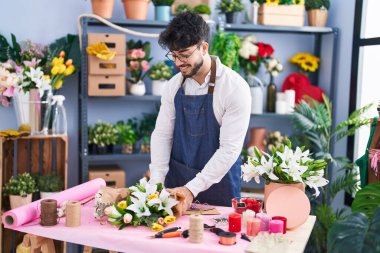 Young hispanic man florist make bouquet of flowers at florist shop
