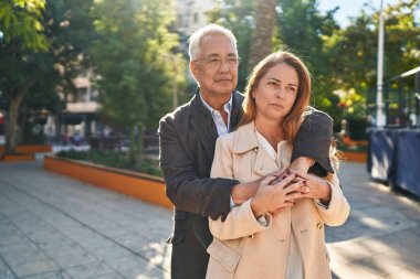 Middle age man and woman couple hugging each other standing with relaxed expression at park