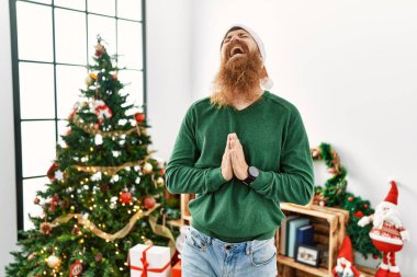 Kızıl saçlı, uzun sakallı, Noel ağacının yanında Noel şapkası takan, elleri bağlı yalvaran ve dua eden, yüzünde umut ifadesi olan çok duygusal ve endişeli bir adam. Yalvarıyor. 