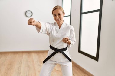 Genç beyaz kadın, spor merkezinde kendine güvenen karate eğitimi alırken gülümsüyor.