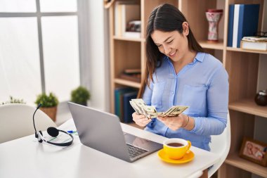 Evde dolar sayan dizüstü bilgisayar kullanan genç bir kadın.