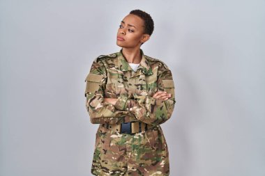 Kamuflaj üniforması giyen güzel Afro-Amerikan kadın kollarını kavuşturmuş, kendinden emin ve ikna olmuş bir şekilde yan tarafa bakıyor. 