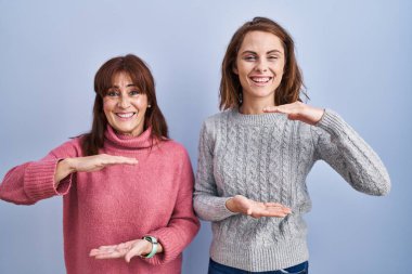 Anne ve kızı mavi arka planda duruyor. Ellerinde büyük ve büyük bir işaret, ölçü sembolü var. Kameraya bakıp gülümsüyor. ölçüm kavramı. 