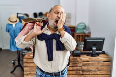Butik dükkanında alışveriş torbaları tutan yakışıklı bir adam. Yarı yüzünü, gözünü ve ağzını elleriyle kapatmaktan yorulmuş esniyor. Yüzüm acıyor.. 