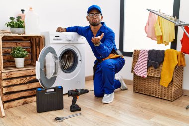 Çamaşır makinesinde çalışan genç Hintli teknisyen kameraya bakıp havada bir öpücük savuruyor ve sevimli ve seksi oluyor. aşk ifadesi. 