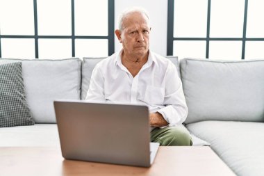 Senior man using laptop at home sitting on the sofa depressed and worry for distress, crying angry and afraid. sad expression. 
