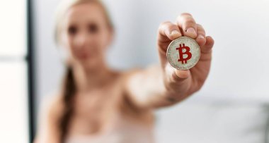 Evdeki kanepede oturan bitcoin tutan beyaz bir kadın.
