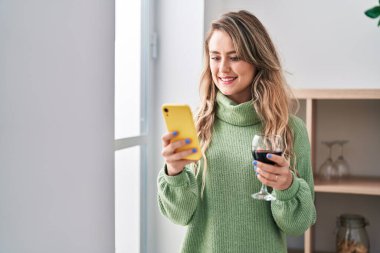 Young woman using smartphone drinking wine at home