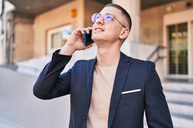 Young hispanic man executive smiling confident talking on smartphone at street