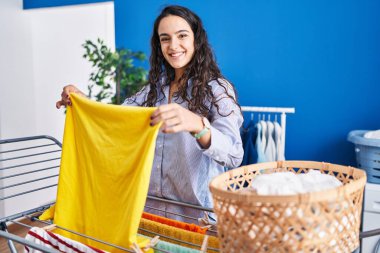 Genç İspanyol kadın gülümsüyor. Çamaşır odasında kendine güveni tam çamaşır ipine asılan kıyafetler.