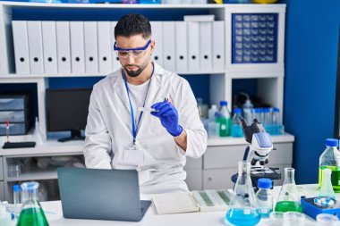 Genç Arap bilim adamı laboratuvarda dizüstü bilgisayar örneği kullanıyor.