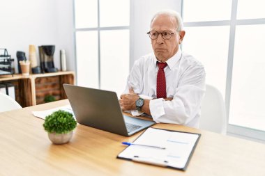 Senior man working at the office using computer laptop skeptic and nervous, disapproving expression on face with crossed arms. negative person. 