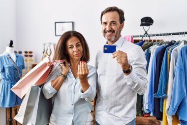 Hispanic middle age couple holding shopping bags and credit card doing italian gesture with hand and fingers confident expression 
