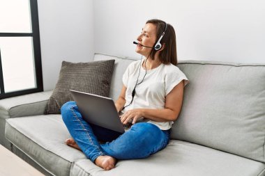 Orta yaşlı İspanyol kadın evde kulaklık takarak kanepede oturuyor.