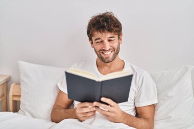 Yatak odasında kitap okuyan genç bir adam.