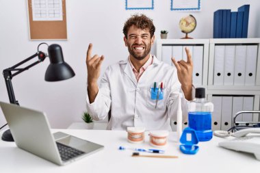 Klinikte çalışan genç İspanyol dişçi deli gibi bağırarak elleri havada rock sembolü yapıyor. Müzik yıldızı. ağır kavram. 