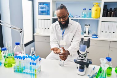 Genç Afrikalı Amerikalı adam laboratuarda dezenfektan jeli kullanan bilim adamı üniforması giyiyor.