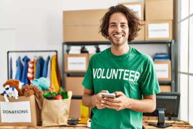 Hayır kurumunda akıllı telefon kullanarak mutlu gülümseyen genç İspanyol gönüllü adam..