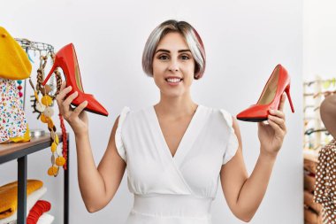 Genç beyaz kadın gülümseyerek giyim mağazasından yüksek topuklu ayakkabı seçiyor..