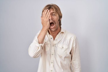 Orta yaşlı bir adam izole edilmiş arka planda duruyor. Yarı yüzünü, göz ve ağzını eliyle kapatmaktan yorulmuş. Yüzüm acıyor.. 