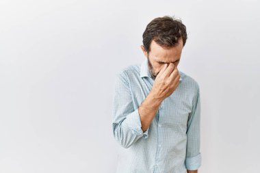 Middle age hispanic man with beard standing over isolated background tired rubbing nose and eyes feeling fatigue and headache. stress and frustration concept. 