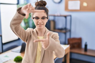 Ofiste çalışan, gözlüklü, gülümseyen, elleri ve parmakları gülen yüzlü genç bir kız. yaratıcılık ve fotoğrafçılık kavramı. 