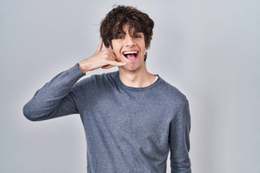 İzole edilmiş arka planda duran genç adam gülümseyerek el ve parmaklarıyla telefon hareketi yapıyor telefonda konuşuyor gibi. iletişim kavramları. 