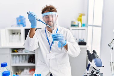 Laboratuvarda çalışan, bilim adamı üniforması giyen İspanyol genç adam.