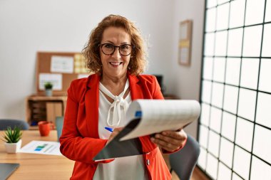 Ofiste çalışırken gülümseyen orta yaşlı beyaz iş kadını.