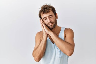 Genç yakışıklı adam izole edilmiş arka planda ayakta uyur. Yorgun düşler kurar, ellerle poz verir ve gözleri kapalı gülümserdi.. 