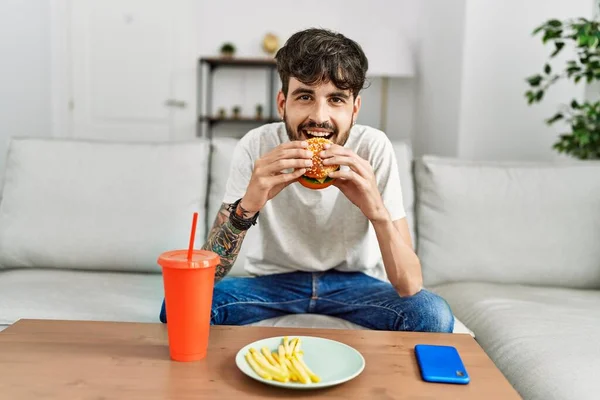 Latin Kökenli Genç Adam Klasik Burger Yiyor Evdeki Kanepede Soda — Stok fotoğraf