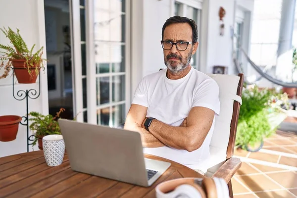 Middle age man using computer laptop at home skeptic and nervous, disapproving expression on face with crossed arms. negative person.